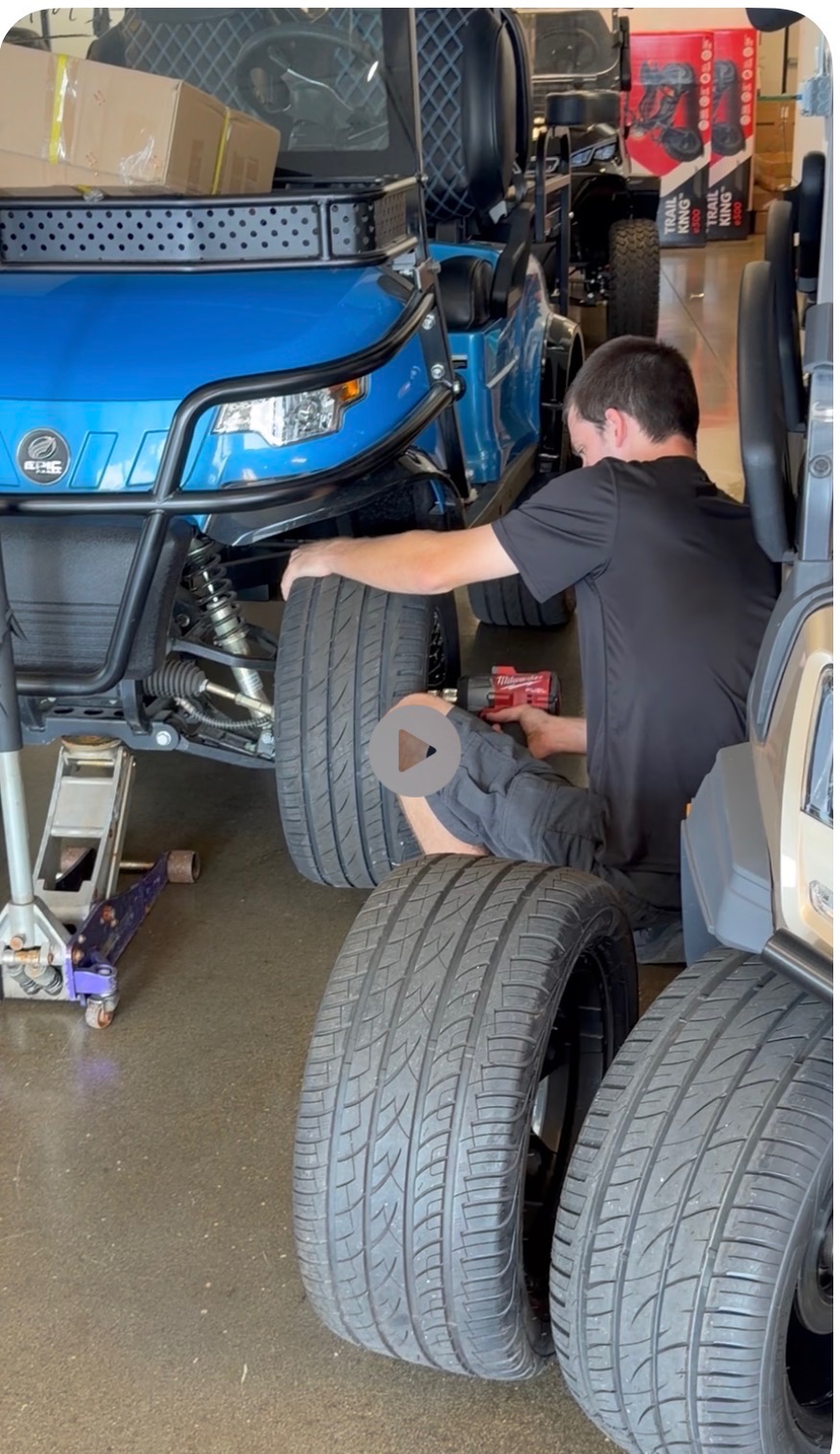 ICON Golf Carts technician working on the wheel assembly of a blue EPIC electric golf cart in the service bay